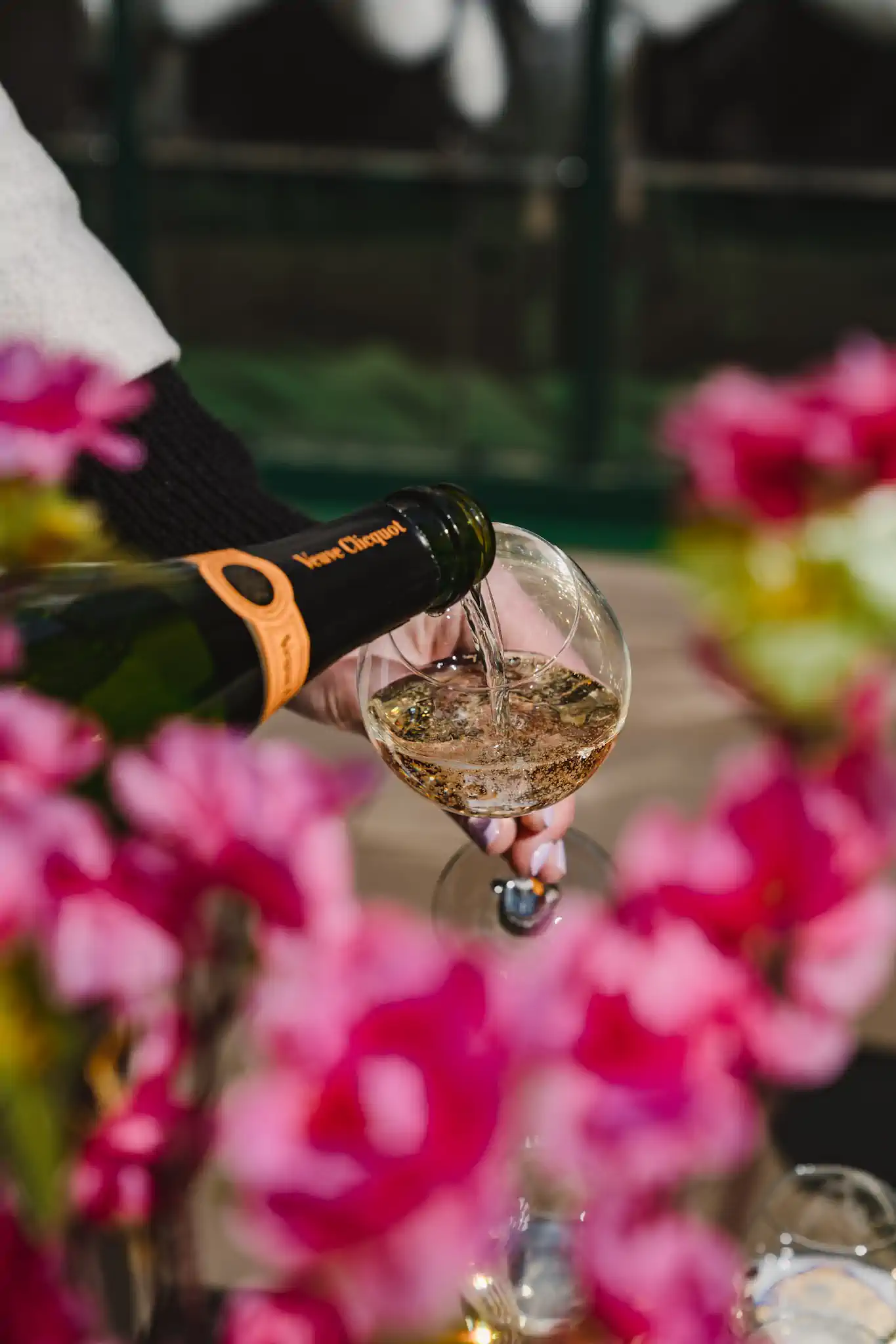 Hand schenkt Veuve Clicquot Rosé-Champagner in Coupette-Glas zwischen pinken Orchideen ein – Villa Kennedy Ostern