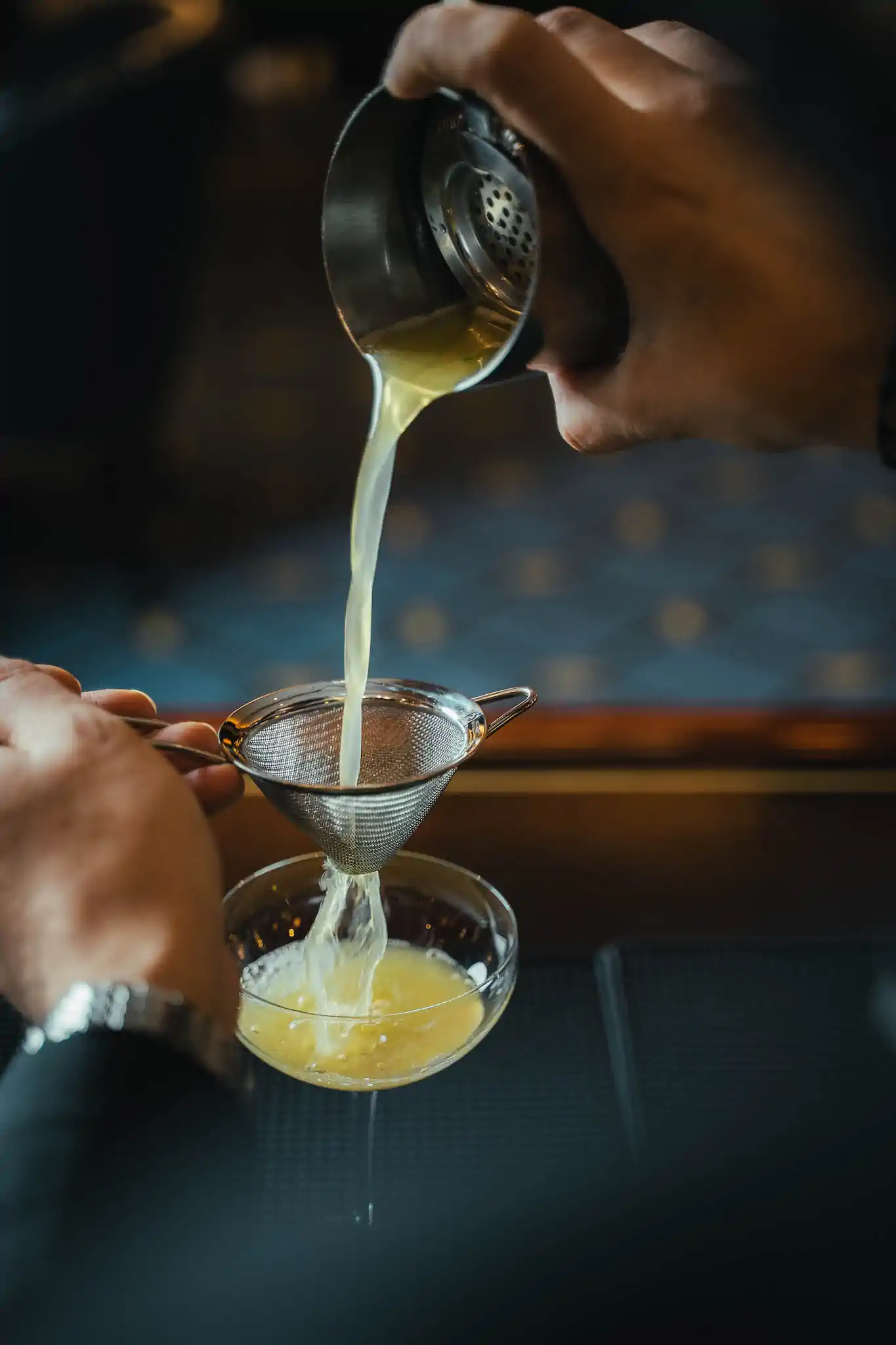 Barkeeper-Hand seiht gelben Sour in Kugelglas mit Crushed Ice und Olive ab – Steigenberger Frankfurter Hof