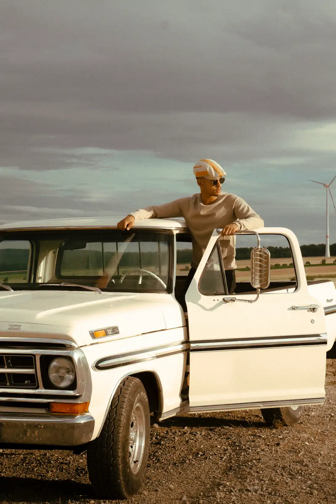 Mann mit Turban und Sonnenbrille an weißem Ford-Oldtimer-Pickup in Feldlandschaft – DANIEL