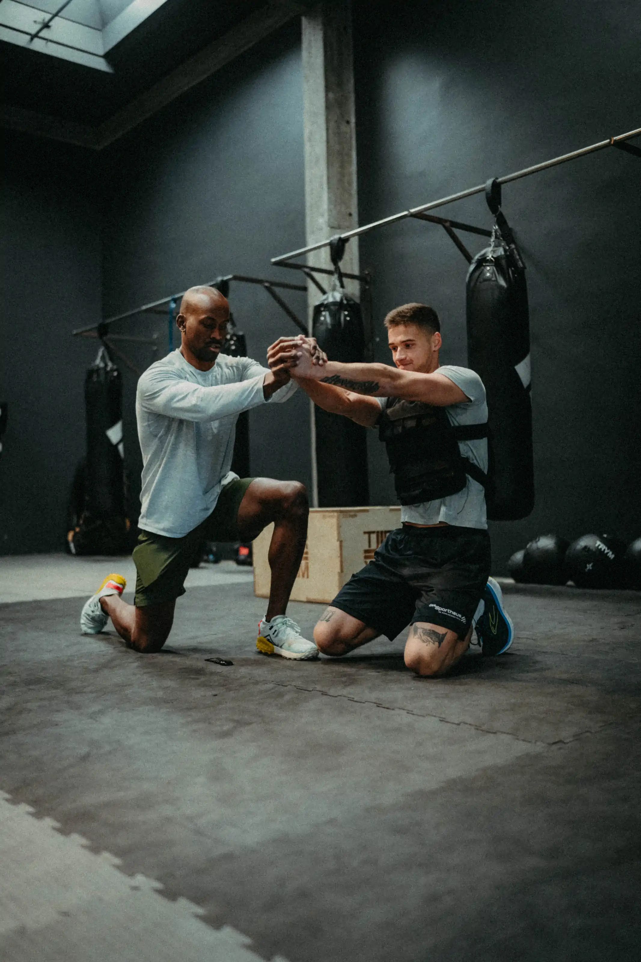 Zwei Sportler beim Fausttraining vor Boxsäcken in dunkler Trainingshalle – ASA Personal Training
