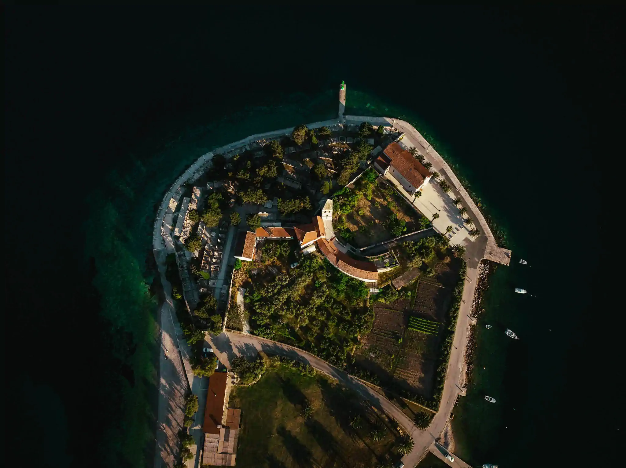 Drohnenaufnahme einer kroatischen Inselspitze mit Leuchtturm, Kirche und Friedhof im dunklen Meer – TPS Kroatien