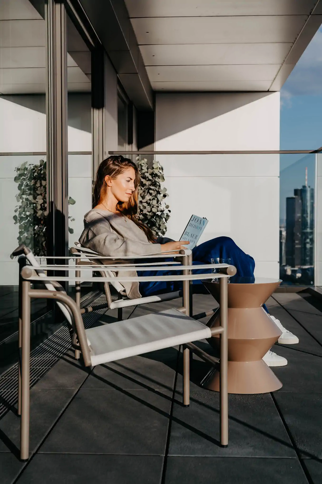 Frau liest Joan-Didion-Buch im LC1-Sessel auf Dachterrasse mit Frankfurter Skyline – One Forty West