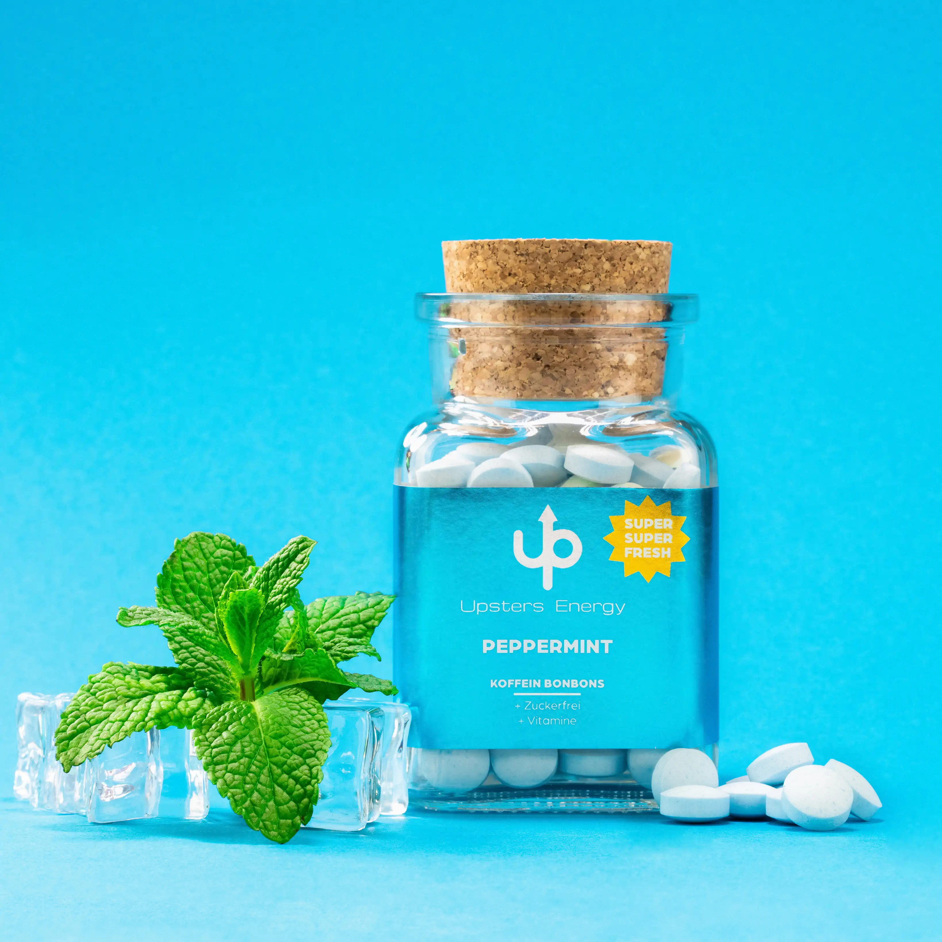 Glasflasche mit weißen Koffein-Bonbons und Korkstopfen vor türkisem Hintergrund mit Minze – Upsters Peppermint