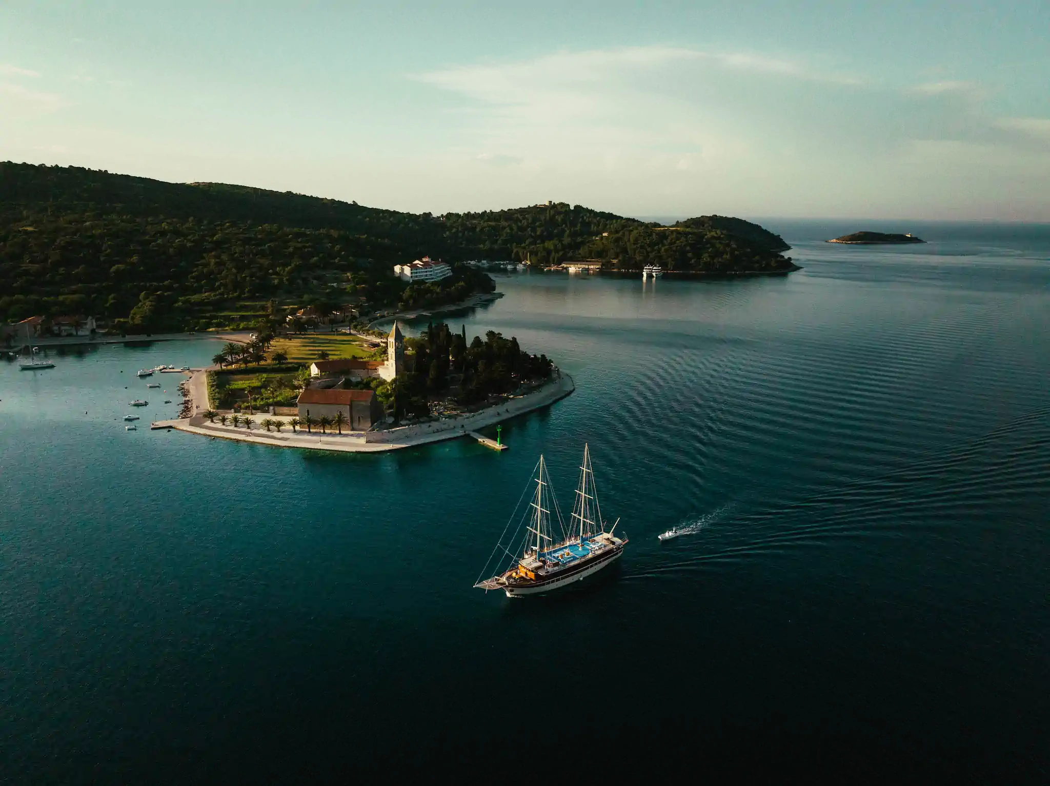 Drohnenaufnahme einer Adriaküste mit Segelschiff, Kirche auf Landzunge und bewaldeten Inseln – TPS Kroatien