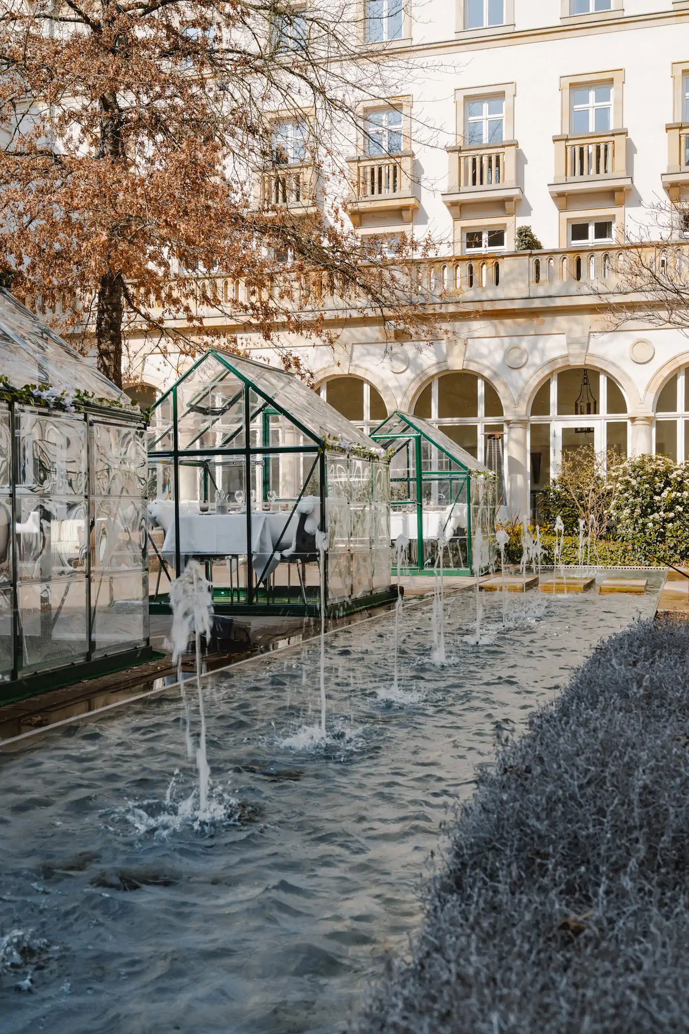 Innenhof mit Pop-Up-Glashäusern und Wasserfontänen vor Villa Kennedy Fassade – Frankfurt