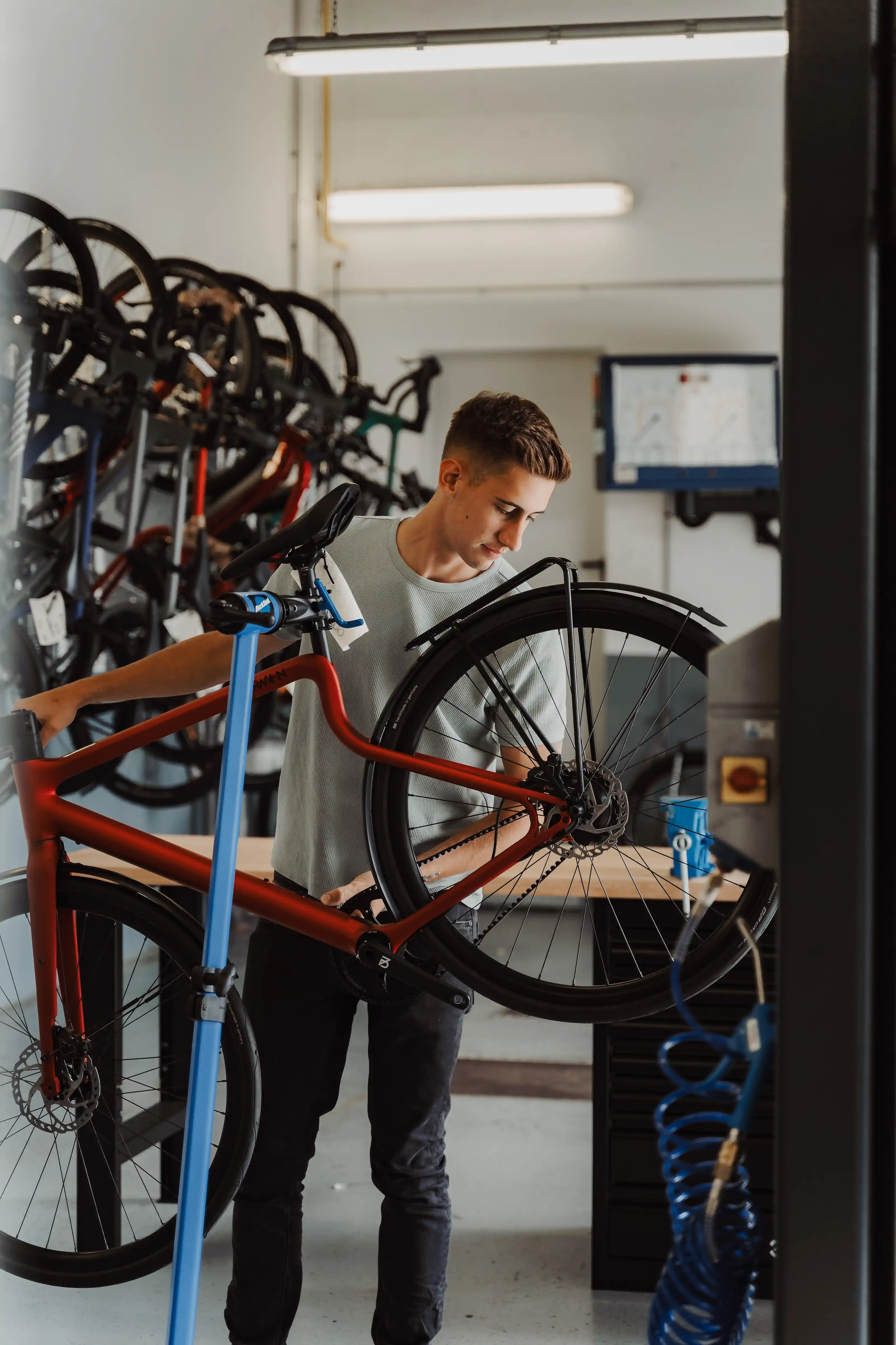 Junger Mechaniker montiert rotes Fahrrad auf blauem Montageständer in heller Werkstatt – KVD Lookbook