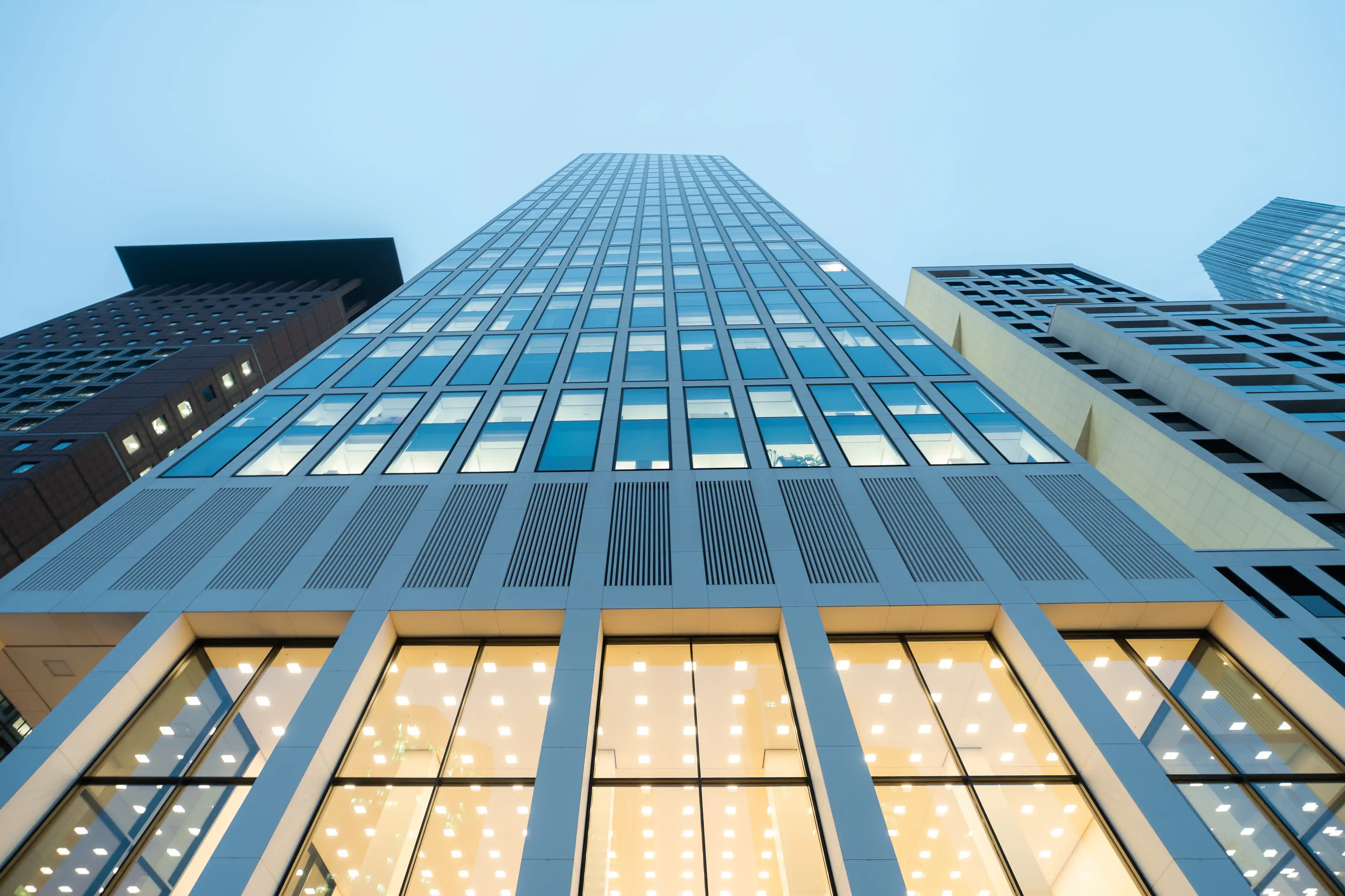 Froschperspektive auf Frankfurter Hochhausfassade mit Lichtern im Erdgeschoss – Architektur Frankfurt
