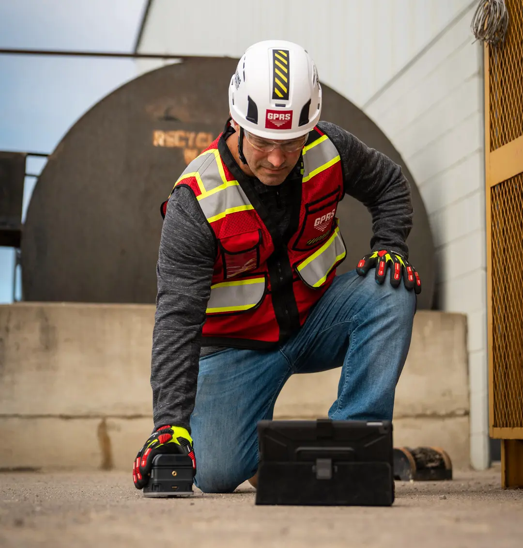 A worker kneels on a concrete pad while scanning with ground penetrating radar.