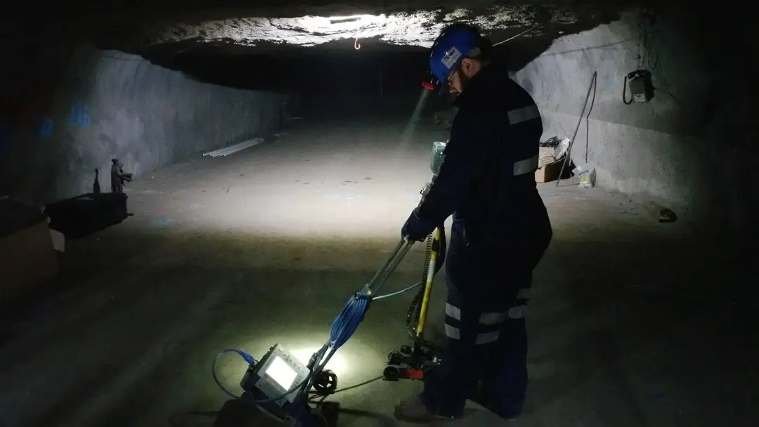 A worker in a mine shaft uses his headlamp to illuminate a GPR scanner.