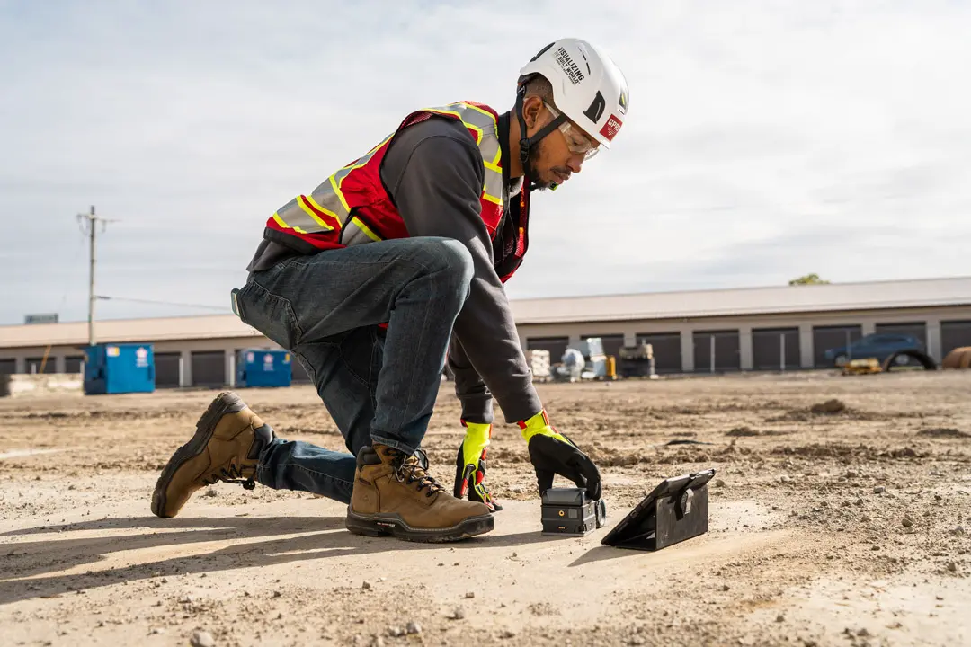 A worker kneels on a concrete pad while using a ground penetrating radar scanner.