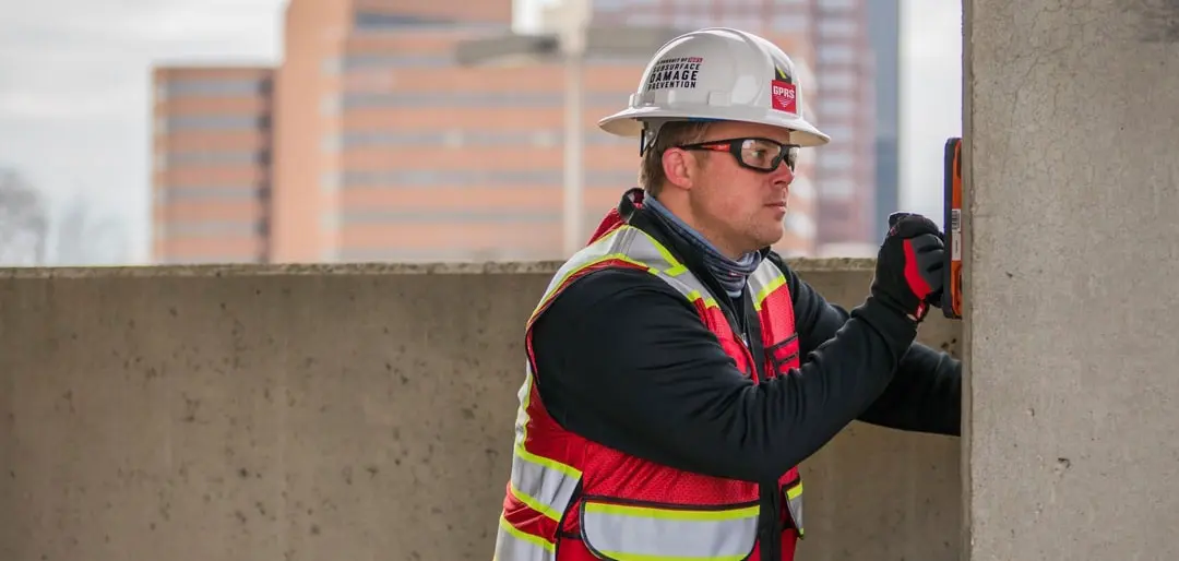 A worker scans a concrete wall with ground penetrating radar.