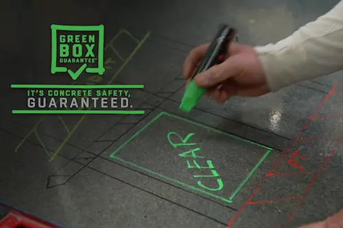 A person marks a green box on a concrete slab.