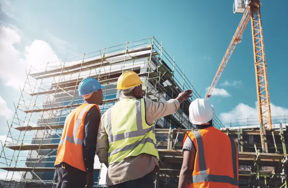 Three construction workers looking up at a building under construction.