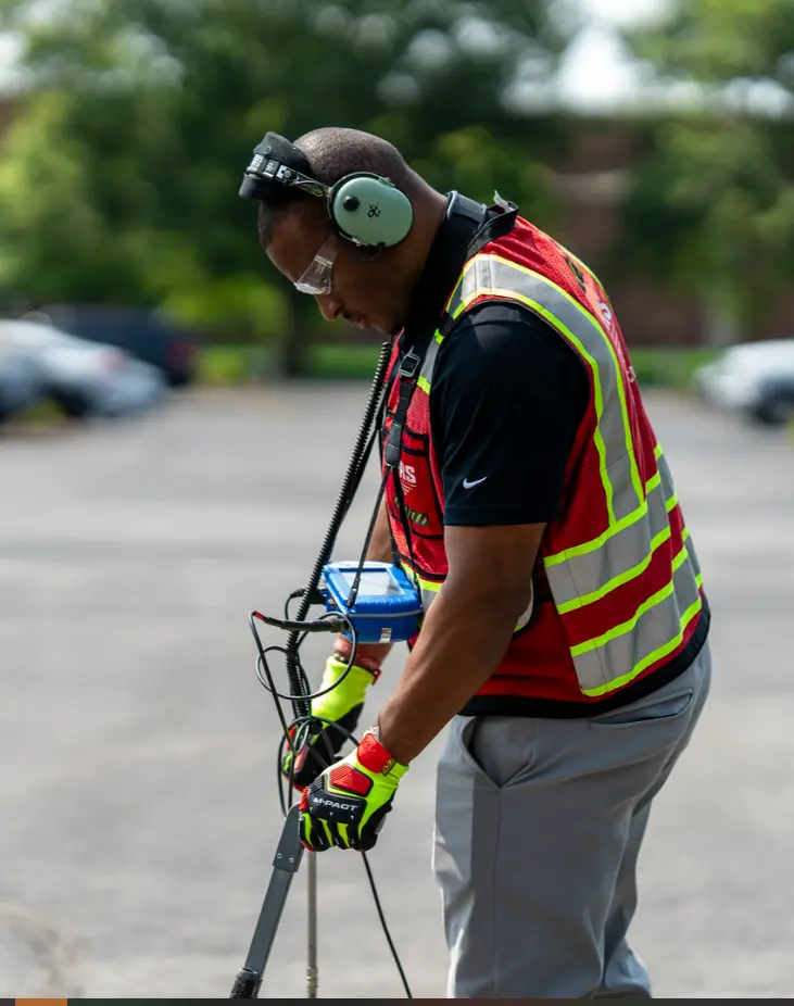 A GPRS Project Manager wearing headphones and utilizing multiple technologies to pinpoint and mark out a water leak. 