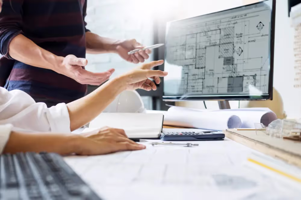 People working with construction documents and pointing at a computer screen.