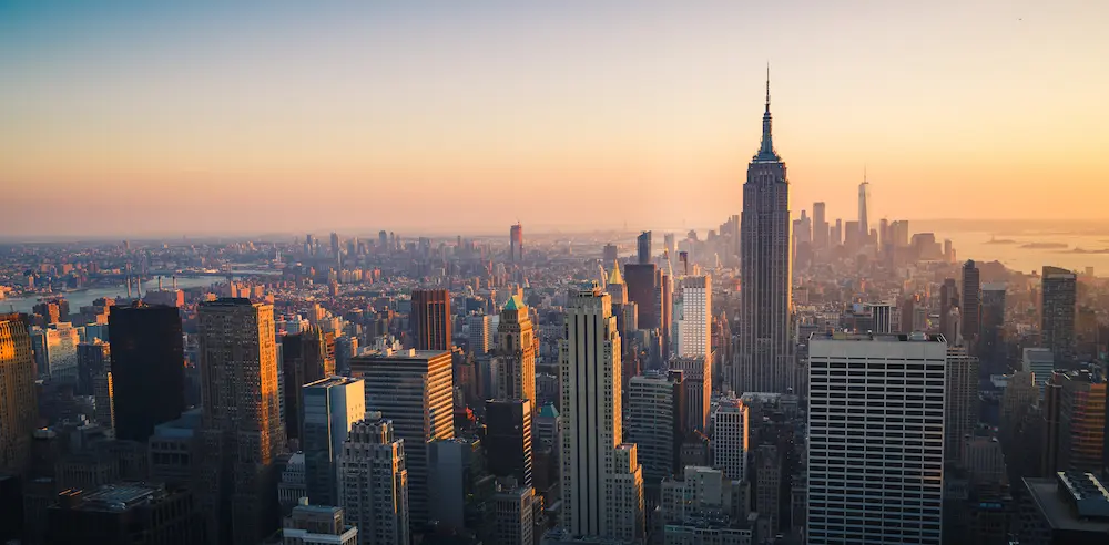 The New York City Skyline at golden hour on a clear day with the Hudson River in the distance.