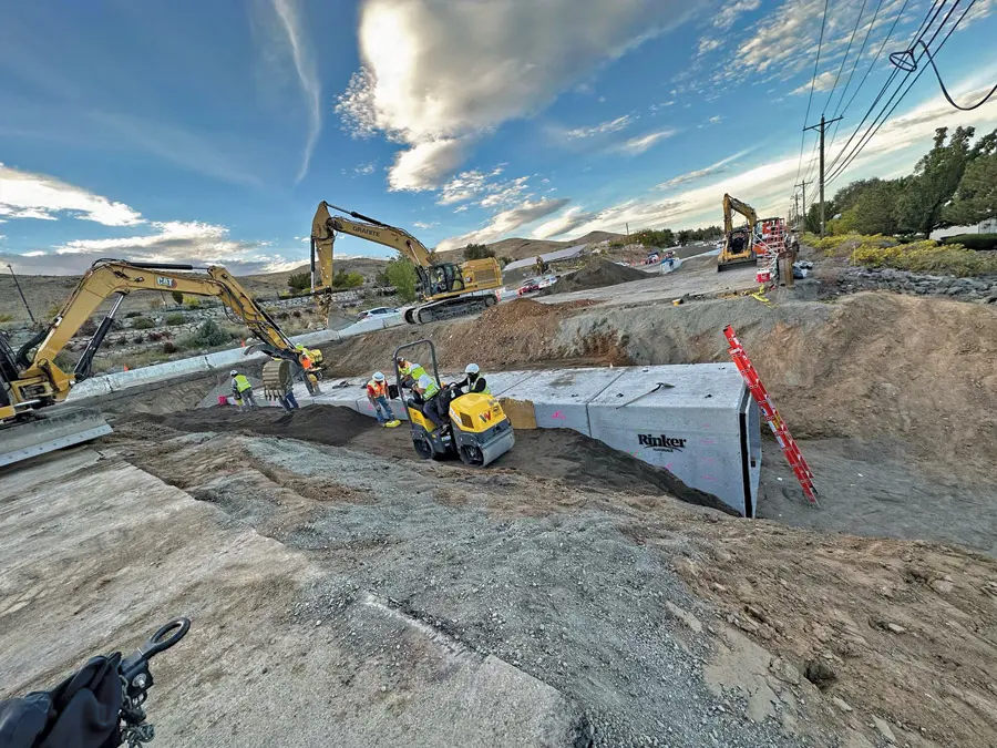 Construction workers and heavy machinery in a trench next to a road construction.