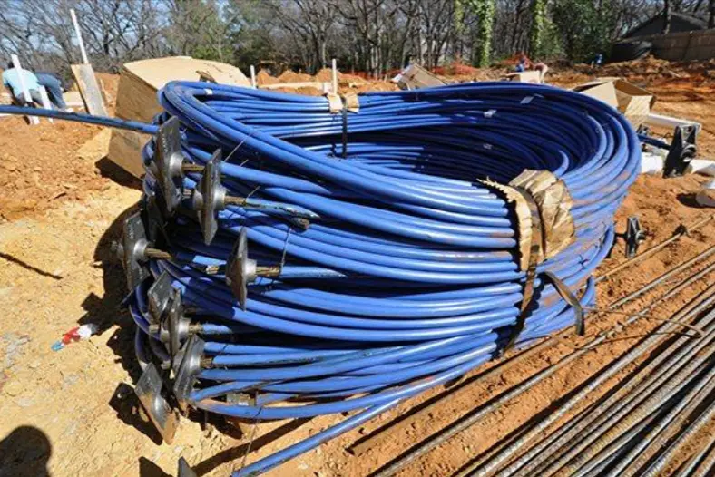 A large bundle of post tension cables on a jobsite, sheathed in blue plastic with the “dead” end already seated in an anchor plate. Below the bundle in the right lower corner, you can see loose rebar, also waiting to be installed.