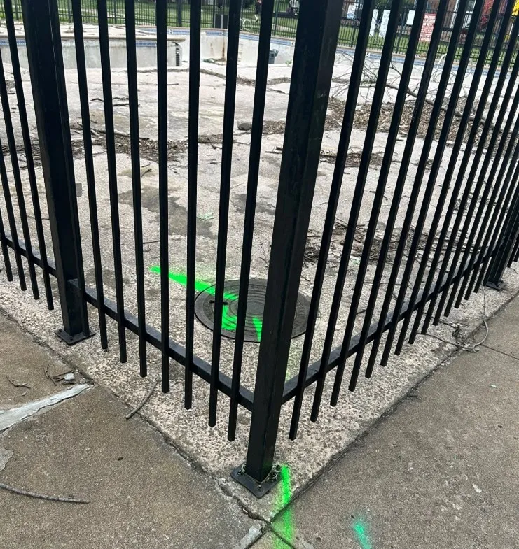 A manhole and outdoor pool inside a gated area with green spray paint marking out the surface to represent underground sewer lines.