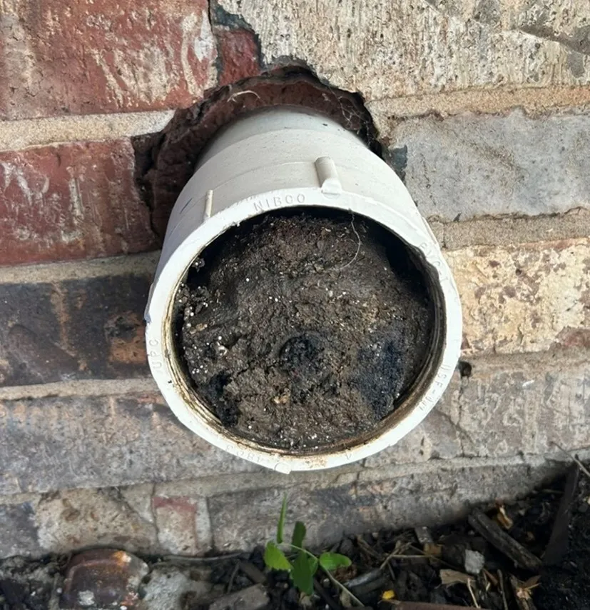 An external clean out extending out of a brick structure that is blocked by dirt