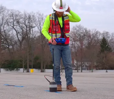 A GPRS Project Manager wearing the proper PPE, including a helmet and red vest, while utilizing an acoustic leak detector, also known as an “elephant foot,” and wearing noise canceling headphones to listen for leaks.