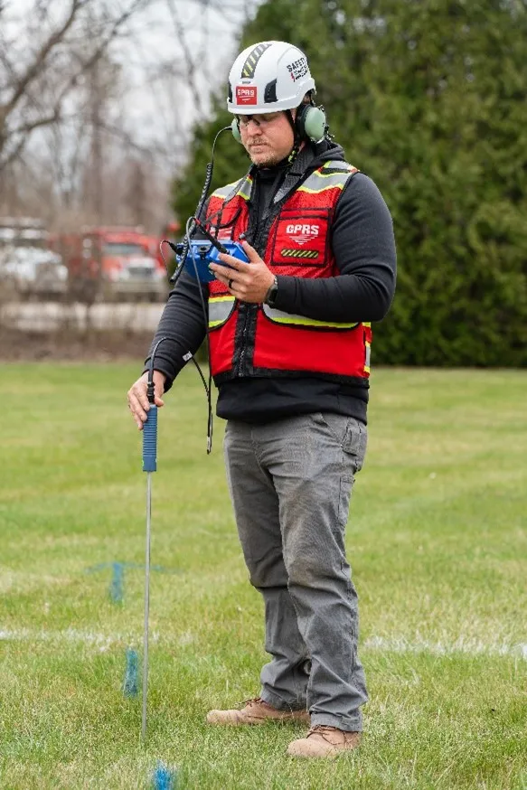 A GPRS Project Manager utilizing a blue, black, and silver leak noise correlator in a grassy field.