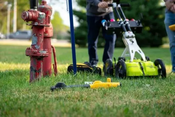 Ground penetrating radar and an electromagnetic (EM) locator in a grassy area to the right of a red sewer cleanout.