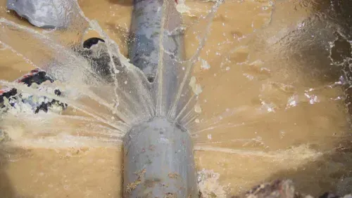 A cracked water pipe with water spraying in many different directions.