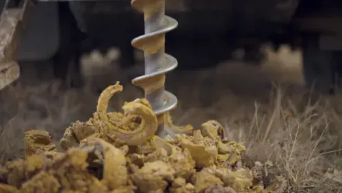 A drill coming out of a muddy area after drilling into the Earth.