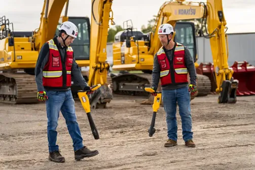 Two GPRS Project Managers utilizing electromagnetic (EM) locators on a job site with dirt floors and two excavators behind them.
