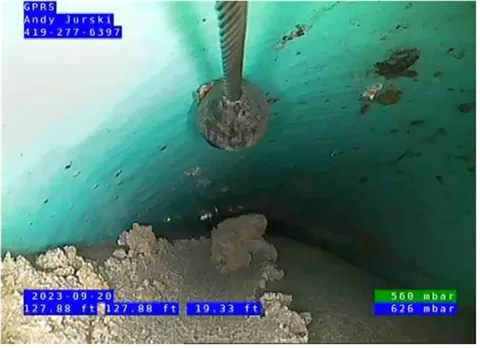 The view of a push camera from inside a pipe with debris at the bottom of the pipe that is a light turquoise color. Data in white text and blue boxes are featured in the bottom right, top left, and bottom left corners.