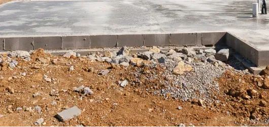 A concrete slab that is placed directly on the ground with light grey rocks around the edges of the concrete.