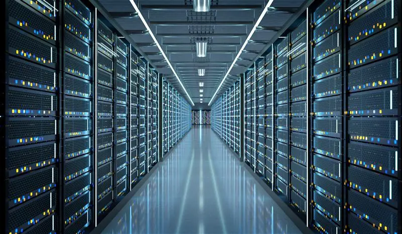 Looking down an aisle inside a data center, with computer equipment lit up on either side.