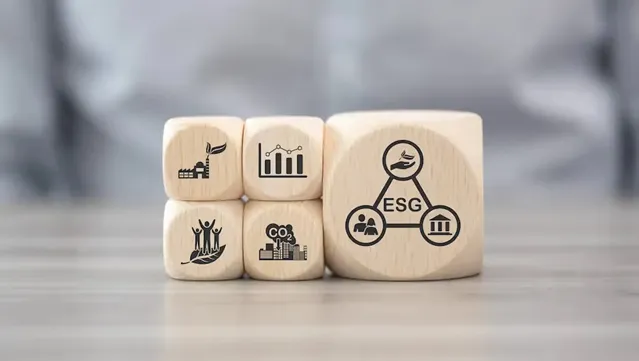 Four wooden cube stacked in two rows of four next to a larger wooden cube, with the letter “ESG” on it. Symbols like stick figures, building, and a graph are shown on the smaller cubes.