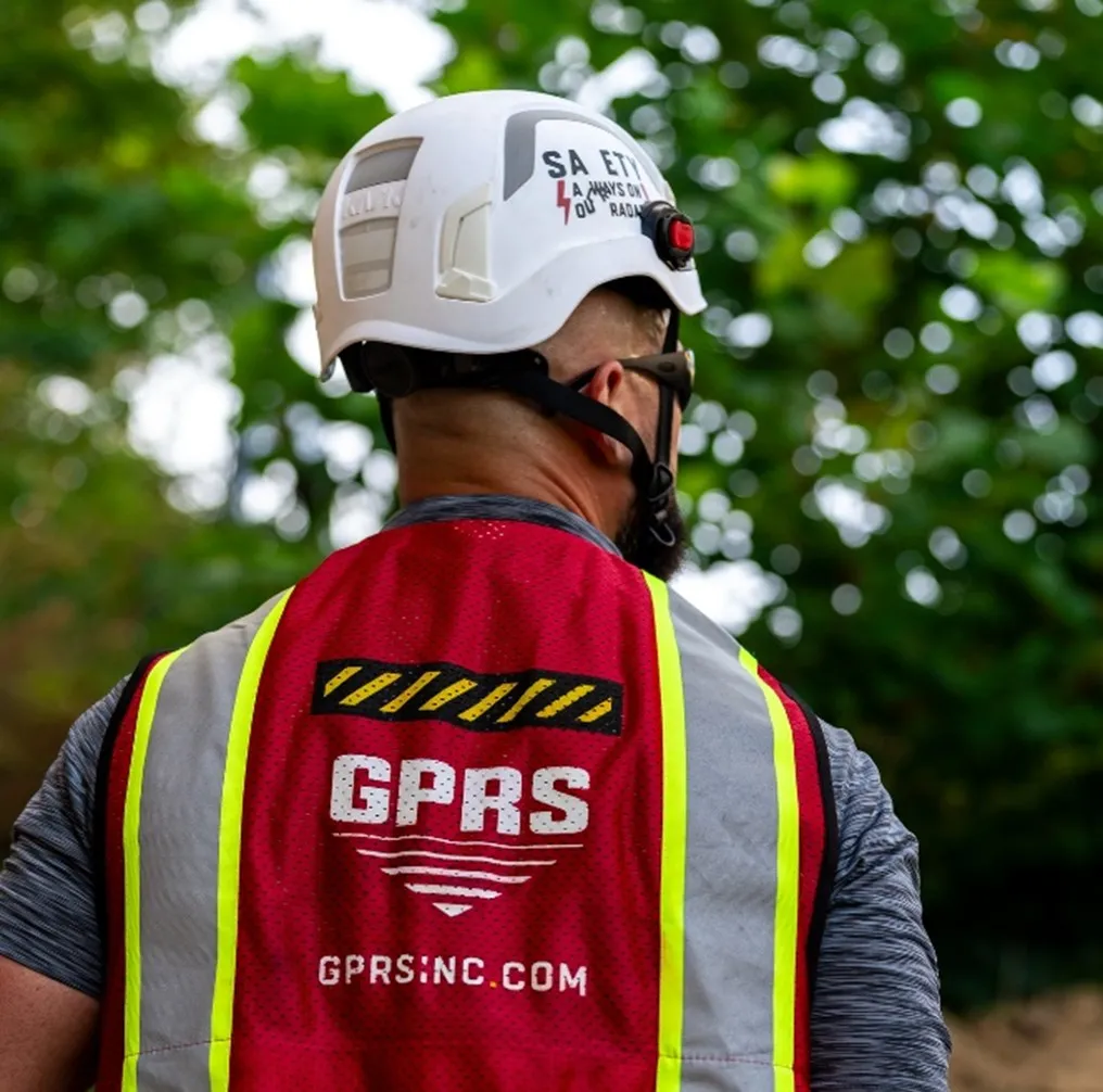 A man wearing a white safety helmet and red vest with “GPRS GPRSINC.COM” on the back over a grey shirt.