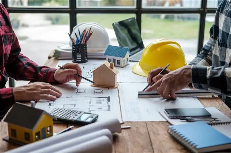A group of engineers working through blueprints and model houses on their desks.