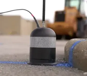 A black plunger-like object with a silver, metal stripe across the center at the end of a pole on cement with blue spray paint under and around it.