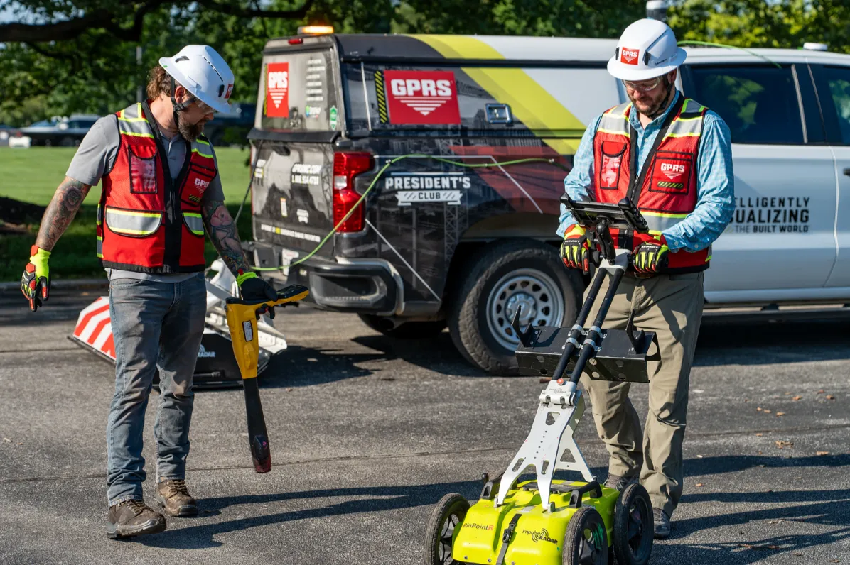 A high speed GPR array is attached to the back of a GPRS truck. In front of that array are two Project Managers: one with a ground penetrating radar cart and one with an electromagnetic locating wand. Both are dressed in red vests and PPE.