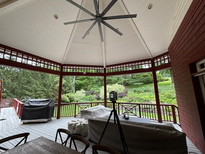 Covered outdoor patio with a white vaulted ceiling and large ceiling fan, surrounded by red wooden railings.