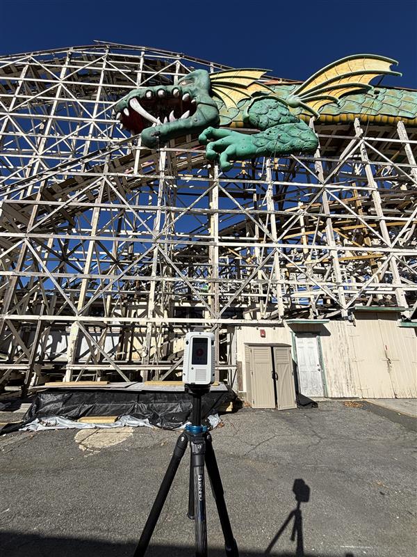 A Leica laser scanner on a tripod placed in front of the Dragon Coaster, a wooden coaster with a green and yellow dragon placed on the track as a tunnel. 