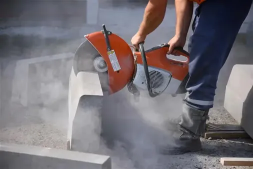 A construction worker operating a large saw as it cuts through a piece of concrete, creating millions of particles of respirable crystalline silica. 