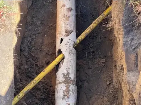 A yellow telecom line intersecting through a cracked pipe