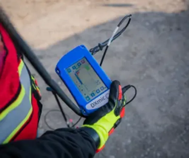 A GPRS Project Manager wearing red, grey, and yellow vests & gloves while holding a blue leak noise correlator. 