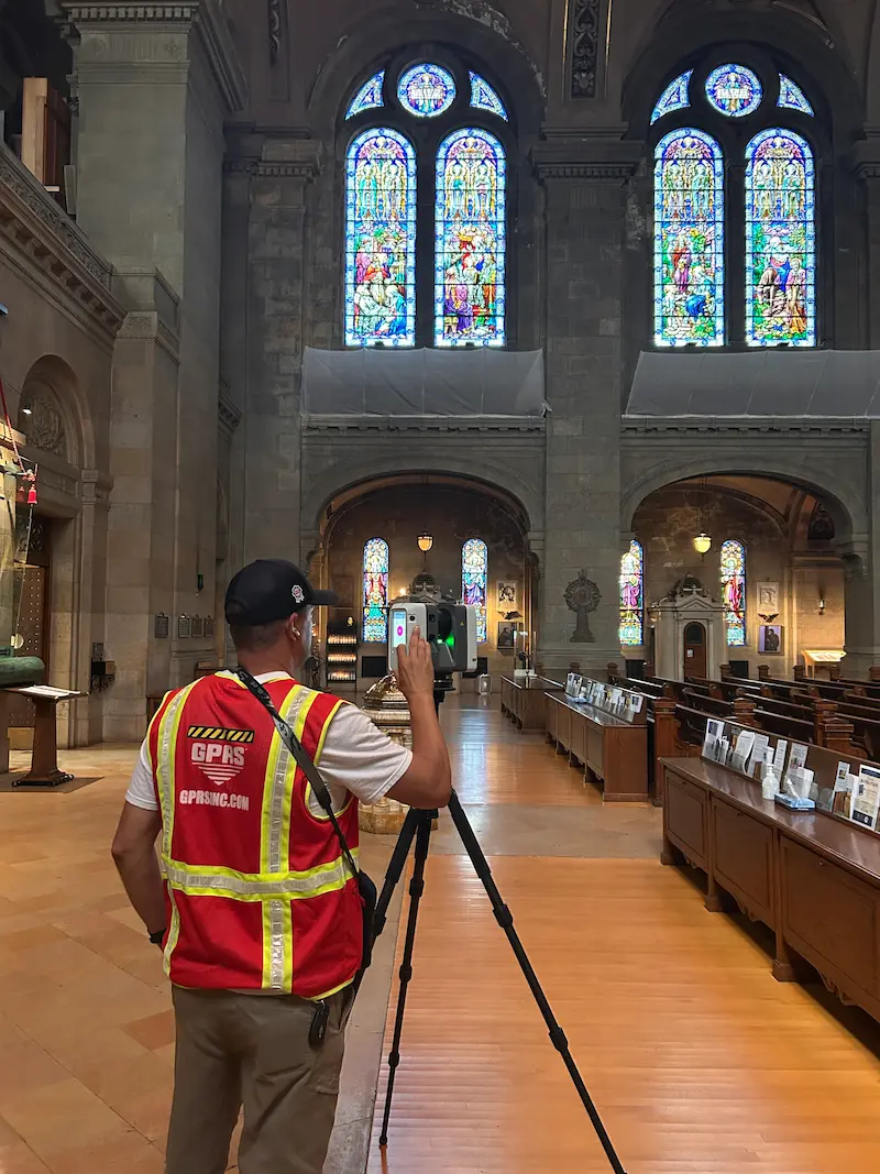 GPRS Project Manager wearing a high‑visibility vest operating a tripod-mounted 3D laser scanner inside the Basilica of Saint Mary with tall stained-glass windows and ornate architectural details.