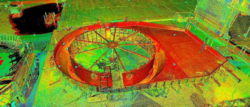 A colorized 3D point‑cloud scan of an industrial construction site showing a large circular steel structure with radial support beams at its center. Surrounding platforms, scaffolding, and equipment are visible, with the point cloud rendering displaying vivid shades of red, yellow, green, and blue to indicate different elevations and surfaces.