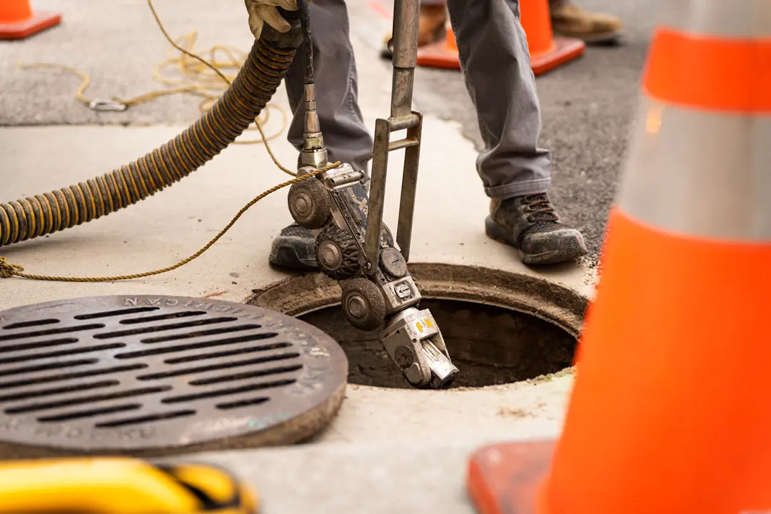 A worker lowers a CCTV crawler robot into an open manhole.