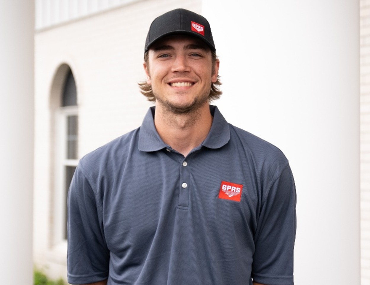 A GPRS Project Manager wearing a grey, long sleeve polo with the GPRS logo on the left chest and a black hat also with the GPRS logo on the left side of the hat.