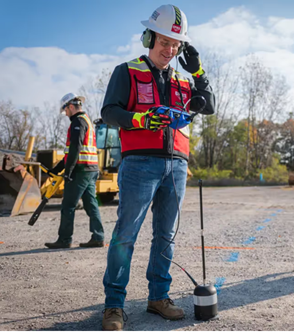 A man in a hard hat and safety vest stands beside a construction site, overseeing leak detection services by GPRS.