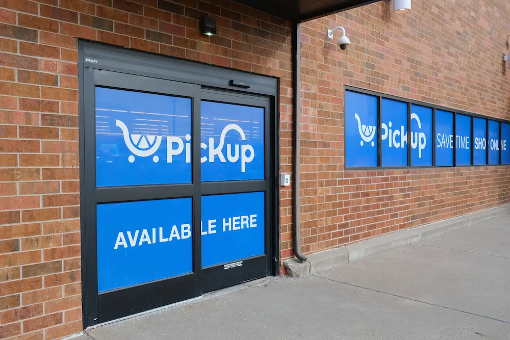 A well-known national grocery retailer advertises their pickup service on signage covering a sliding door and windows on a brick building.