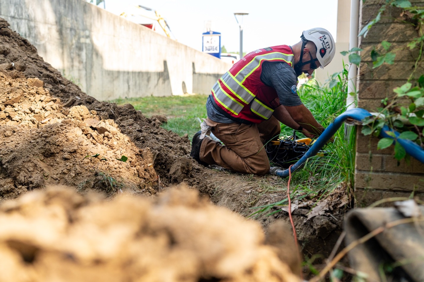 A GPRS Project manager kneels above a trench while locating utilities.